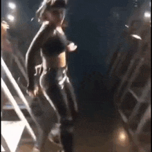 a woman in a crop top and black pants is dancing on a stage .