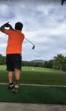 a man in an orange shirt swings a golf club at a golf ball