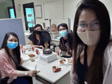 a group of people wearing face masks are sitting around a table with a cake and kfc boxes