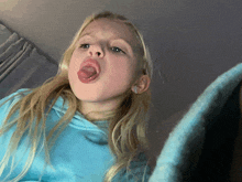 a little girl with her tongue out wearing a blue sweatshirt