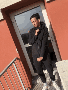 a young man in a black hoodie stands in front of a glass door