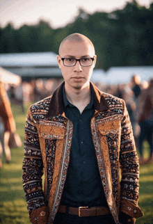 a man wearing glasses and a colorful jacket stands in the grass