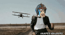 a man in a suit with a monkey mask on his face is running in a field with a plane flying in the background