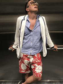 a man wearing a white jacket and red shorts is standing in an elevator