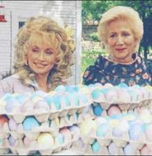 two women standing next to each other holding trays of easter eggs