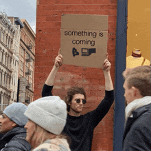 a man holding a sign that says something is coming