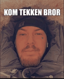 a man with a beard wearing a black hat and a jacket with the words kom tekken bror written above him