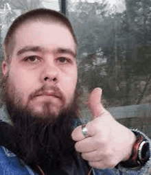 a man with a beard and a watch is giving a thumbs up sign .