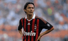 a soccer player wearing a red and black striped jersey is standing on a field .