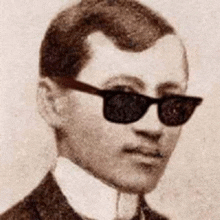 a man in a suit and tie is wearing sunglasses and looking at the camera .