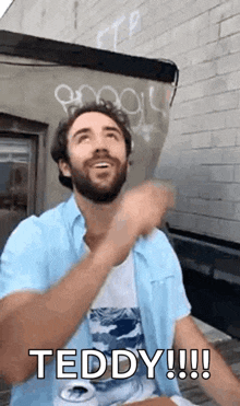 a man with a beard is sitting at a table with a can of beer in front of a brick building .