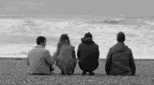 a group of people are sitting on the beach looking at the ocean in a black and white photo .