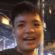 a young man is smiling at the camera while standing in front of a pole .