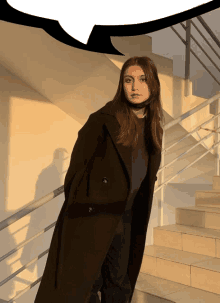 a woman in a long black coat is standing on stairs