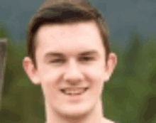 a close up of a man 's face with trees in the background smiling .