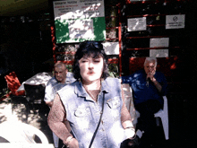 a woman in a denim vest is standing in front of a sign that says ' no smoking ' on it