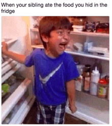 a boy in a blue nike shirt is standing in front of a fridge