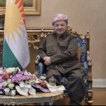 a man wearing a turban sits in a chair with flowers on a table