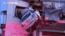 a car that has crashed into a building with euronews written on the bottom .