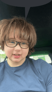 a young boy wearing glasses and a blue shirt looks at the camera