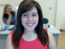 a woman in a red tank top smiles in front of a computer monitor