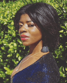 a woman wearing a blue dress and earrings is standing in front of a bush .