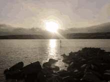 the sun shines brightly over a body of water with rocks in the foreground