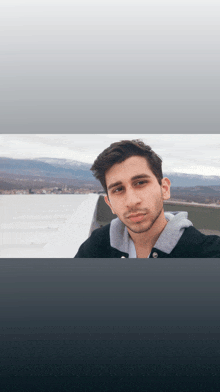 a young man in a black jacket stands on a rooftop looking at the camera