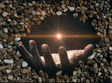 a hand is reaching out towards the sun in a heart shaped rocky area