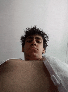 a young man with curly hair looks at the camera while wearing a white towel