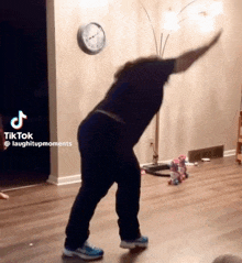 a person is dancing in a living room with a clock on the wall behind them .