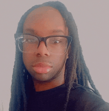 a man wearing glasses and dreadlocks looks at the camera