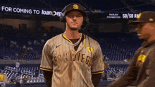 a baseball player wearing headphones and a san diego jersey is standing on the field talking to another player .