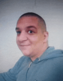 a close up of a man 's face with a shaved head wearing a blue hoodie .