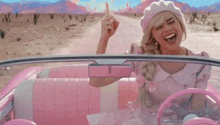 a woman in a pink dress is driving a pink car and giving a middle finger .