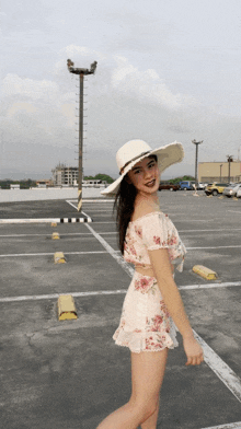 a woman wearing a straw hat and a floral dress stands in a parking lot