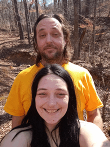 a man and a woman are posing for a picture in the woods and the man is wearing a yellow shirt