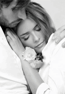 a black and white photo of a man hugging a woman with a white rose on her wrist