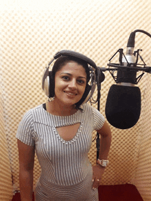 a woman wearing headphones and a watch stands in front of a microphone