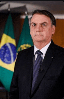 the president of brazil is wearing a suit and tie and standing in front of a flag .