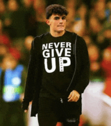 a man wearing a black shirt that says never give up is walking on a field .