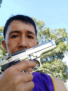 a man in a purple tank top is holding a gun in front of his face