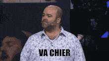 a bald man with a beard stands in front of a microphone and says va chier