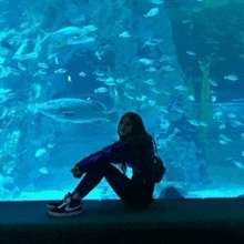 a woman sits in front of a large aquarium filled with fish