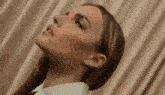 a close up of a woman 's face with a curtain behind her .