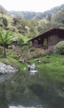 a house sits in the middle of a lush green hillside with a pond in front of it