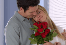 a man kisses a woman on the forehead while holding a bouquet of red roses