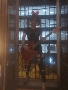 a girl with pigtails and glasses holds a red guitar