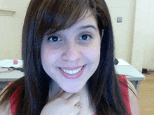 a woman in a red tank top smiles with her hand on her chin