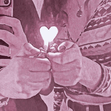 a person is holding a heart shaped object in their hands while taking a selfie with a cell phone .